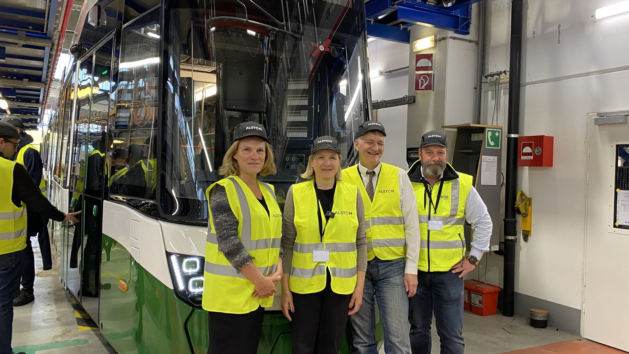 Eine Gruppe von vier Personen steht vor einer neuen Straßenbahn von Graz.
